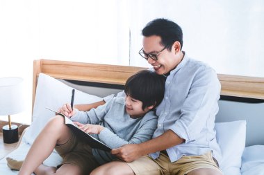 Baba ve oğul yatakta oturup ödev yapıyor bir kitap yazıyor, baba oğluna gülümseyerek yazmayı öğretiyor..