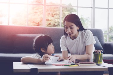 Anne öğretmen, kızına ev ödevlerini yapıyor. Evdeki oturma odasındaki kanepenin boyama kitabında..