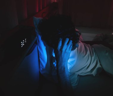 Uykusuzluk çeken uykusuz bir adam gecenin bir yarısı çalar saatle yatağında uyumakta sorun yaşıyor..