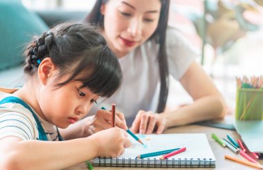 Anne Öğretmen, kızına, evdeki oturma odasındaki kanepenin boyama kitabında ödev yapmayı öğretiyor. Aile dayanışması kavramı için.