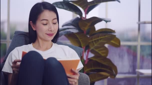 Mujer China Está Leyendo Cuaderno Naranja Relajándose Sofá Casa — Vídeo de stock