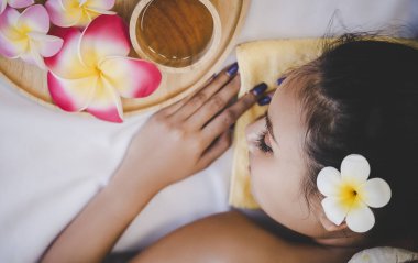 Kadın masaj yatağında rahatlıyor aromaterapi yağı ve kaplıca ve güzellik konsepti için çiçek üst görünümü ile..