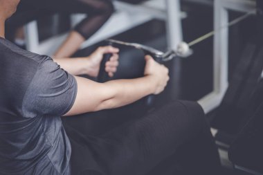 Erkek sporcu spor salonundaki bir fitness makinesine ağırlık veriyor.