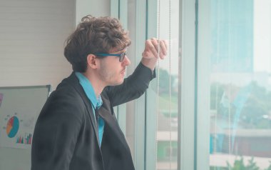 Beyaz iş adamı endişeli bir yüz ifadesiyle pencereden dışarı bakıyor..
