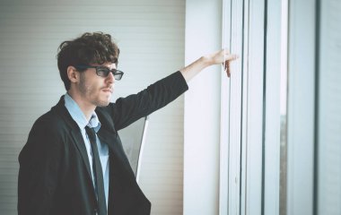 Beyaz iş adamı endişeli bir yüz ifadesiyle pencereden dışarı bakıyor..