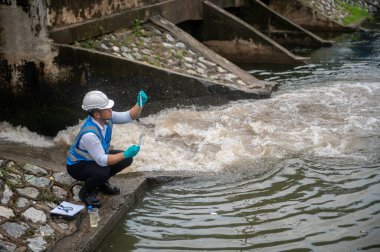 Atık su arıtma işçisi bir kamu kuyusundan su örnekleri topluyor