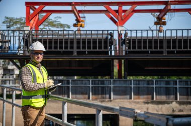 Güneşli alan denetimi sırasında hidrolik su kontrol yapısına güvenle bakan mühendis.