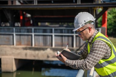 Saha mühendisi endüstriyel su yönetim tesisinin dış denetimi sırasında notlar alıyor.