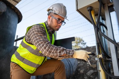 Profesyonel elektrik mühendisi açık hava endüstriyel tesisinde kontrol paneli bakımı üzerinde çalışıyor.