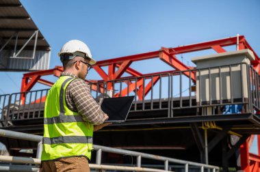 Profesyonel mühendis endüstriyel şantiyedeki hidrolik altyapı operasyonlarını incelemek için dizüstü bilgisayar kullanıyor