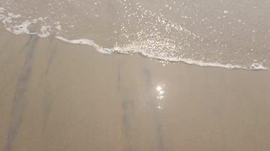 Küçük deniz dalgaları, deniz kumsalının kumları, suda güneşin yansıması.