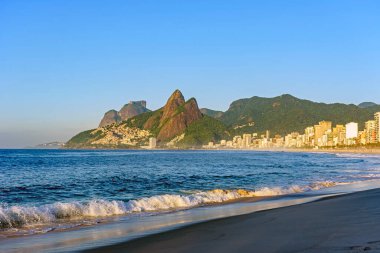 Rio de Janeiro 'daki Ipanema plajında şafak vakti etrafındaki binalar ve dağlarla birlikte hala boş.