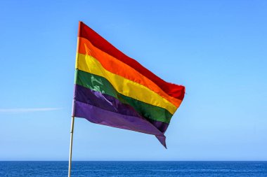 Lbgtq+ flag in the blue sky of the city of Rio de Janeiro, Brazil with sea in background