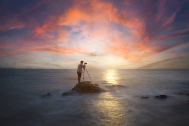 Doğa fotoğrafçısı, gün batımında sahilde taş bir arka plan. 