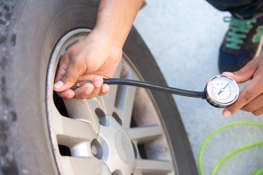 Asyalı adam hava basıncını kontrol ediyor ve arabasının lastiklerini dolduruyor.