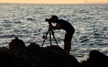 Doğa fotoğrafçısı, gün batımında sahilde taş bir arka plan.