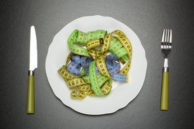 Beyaz tabak çatal ve bıçak ile tabloda bir sarı, mavi, yeşil ve beyaz şerit santimetre ile