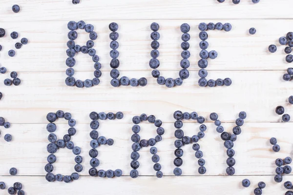 Word blueberry written letters with blueberries on white wooden