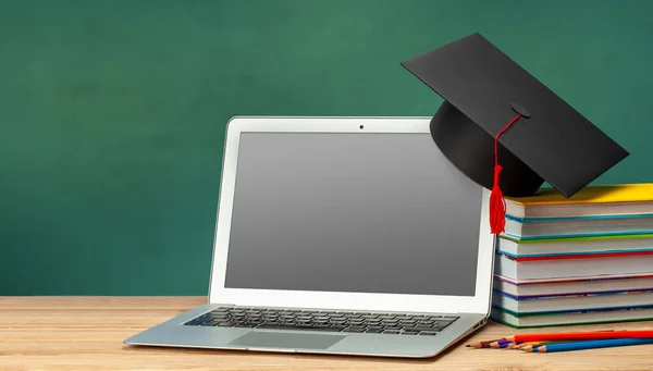 Educación en línea. Enseñanza a distancia en casa. Laptop y pila de libros con sombrero de graduado — Foto de Stock