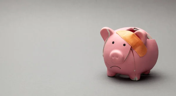 Broken piggy bank with beige adhesive on gray background — Stock Photo, Image