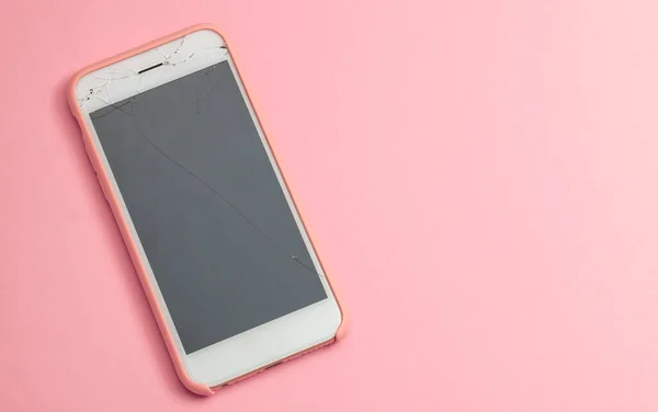 Telefone quebrado com rachadura no vidro de exposição no fundo rosa. Espaço de cópia para texto. — Fotografia de Stock