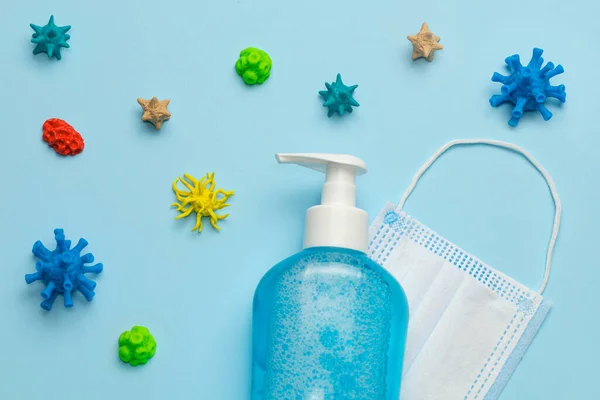 Protezione da virus. Virus intorno disinfettante mano e maschera medica su sfondo blu — Foto Stock