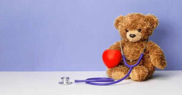 Teddy bear with a stethoscope and a heart on a purple background. Family doctor or pediatrician concept. Template Copy space for text