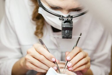 Bir kız, salgın sırasında kirpiklerini uzatma prosedürünü uygular. Elinde aletler olan bir usta.