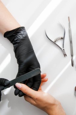 Siyah vinil eldivenli bir usta beyaz bir kıza manikür yapıyor. Çivi çakarak çivi şekillendirmek
