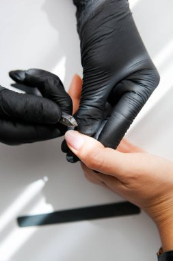 Siyah eldivenli bir usta bir kız için kerpetenle klasik bir manikür yapar. Beyaz ve sarı yüzüklü kadın elleri