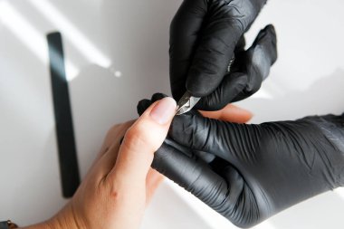 Siyah eldivenli bir usta bir kız için kerpetenle klasik bir manikür yapar. Beyaz ve sarı yüzüklü kadın elleri