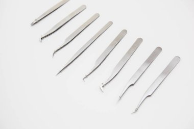 Kirpik uzatma ve kaş tasarımı için araçlar. Beyaz arka planda gümüş renkli kozmetik cımbızlar