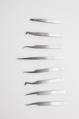 Kirpik uzatma ve kaş tasarımı için araçlar. Beyaz arka planda gümüş renkli kozmetik cımbızlar