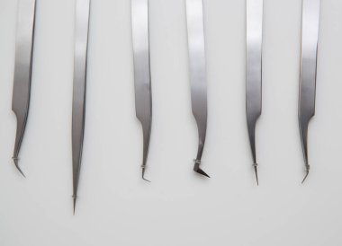 Kirpik uzatma ve kaş tasarımı için araçlar. Beyaz arka planda gümüş renkli kozmetik cımbızlar