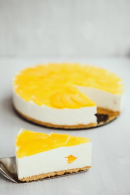 Açık arkaplanda meyveli sarı dolgulu klasik ev yapımı cheesecake dilimi.