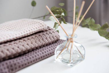 Beyaz arka planda bej ve kahverengi tonlarda pahalı lüks havlular, cam aroma yayıcı. Açık renkli fotoğraf. Temizlik ve rahatlama.