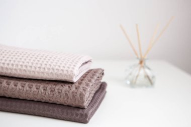 Beyaz arka planda bej ve kahverengi tonlarda pahalı lüks havlular, cam aroma yayıcı. Açık renkli fotoğraf. Temizlik ve rahatlama.