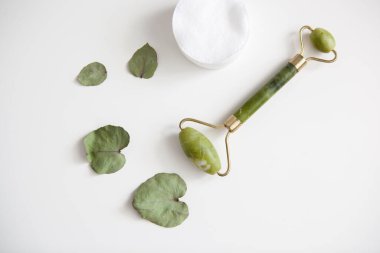 Yeşil yüz masajı silindiri, beyaz pamuk pedler, beyaz arka planda okaliptüs yaprakları.