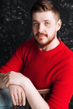 Kızıl saçlı, kırmızı sakallı, genç beyaz bir adam. Kırmızı kazaklı. Elleri olan bir portre.