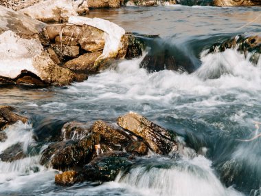 the flow of a stormy river over rocks, clear blue water
