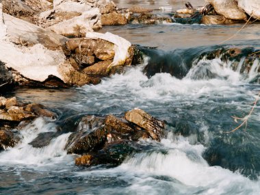 the flow of a stormy river over rocks, clear blue water