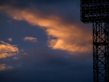 Futbol sahasının silueti turuncu ve mor bir günbatımının arka planında.