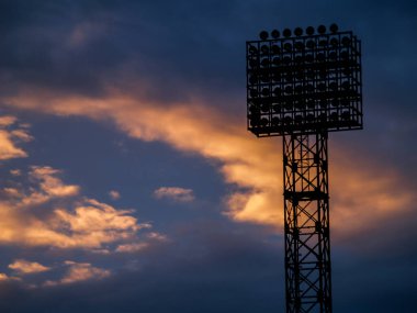 Futbol sahasının silueti turuncu ve mor bir günbatımının arka planında.