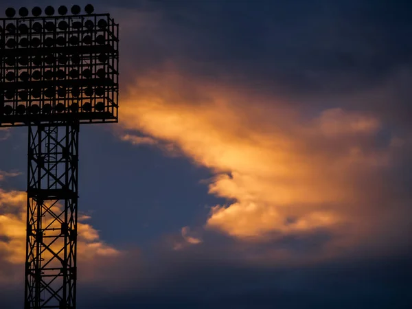 the silhouette of a football field spotlight on the background of an orange and purple sunset