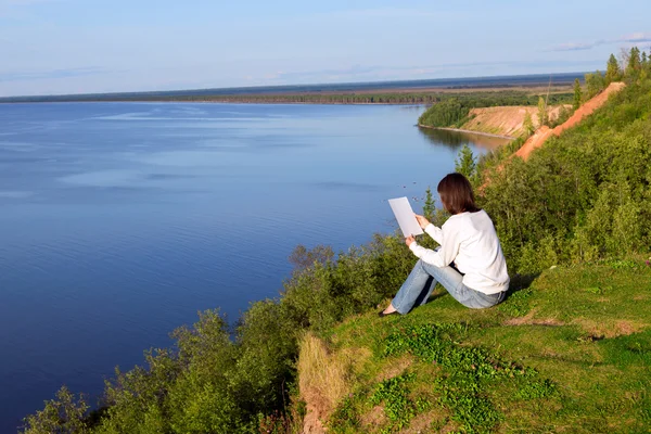 Kağıt boş levha ile göl kıyısında oturan genç kadın — Stok fotoğraf