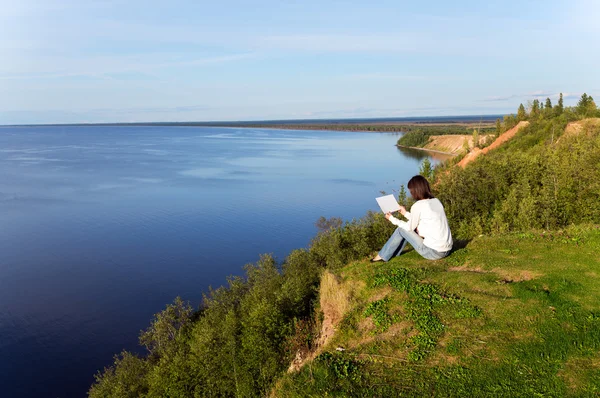 Kağıt boş levha ile göl kıyısında oturan genç kadın — Stok fotoğraf
