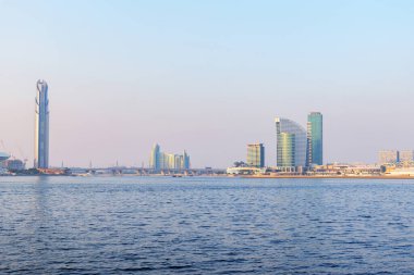 Dubai, BAE. 2 Kasım 2025. Dubai Creek Limanı 'ndan Dubai Festival Şehir Merkezi' ne kadar olan mesafede. Modern rıhtım mimarisi, durgun su, berrak mavi gökyüzü ve Dubai 'nin yumuşak akşam ışığı.