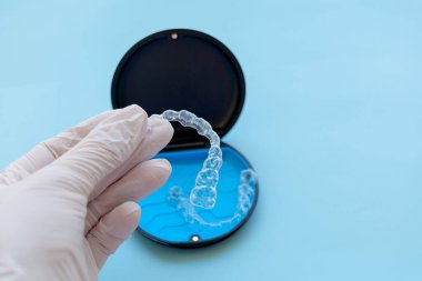 Şeffaf hizalayıcı, eldivenli bir elle dikkatlice tutularak, arkasında da dava, hijyenik tutuş ve günlük diş muayenehanesinde kullanılan çağdaş ortodontik çözümleri vurguluyor