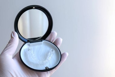 Elinde şeffaf bir hizalayıcının dosyasıyla detaylı bir yakın çekimi var. Netlik, hijyen ve çağdaş diş düzeltme cihazlarının rafine tasarımı