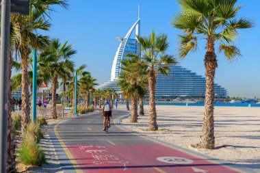 Dubai sahilinin yanındaki palmiye ağaçlarının arasından geçen açık işaretli kırmızı bisiklet yolu. Aktif bir kıyı yaşam tarzı için bisiklet, koşu, yürüyüş ve keyif için popüler bir nokta